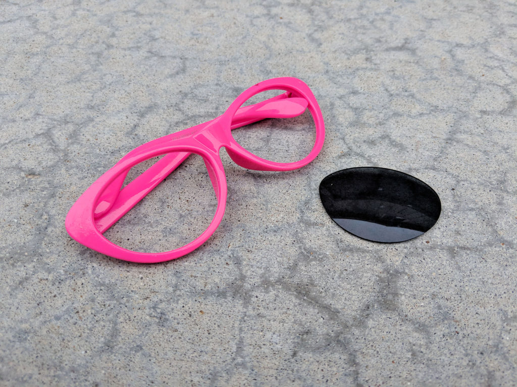 Pink-framed sunglasses with no lenses next to an individual dark lense