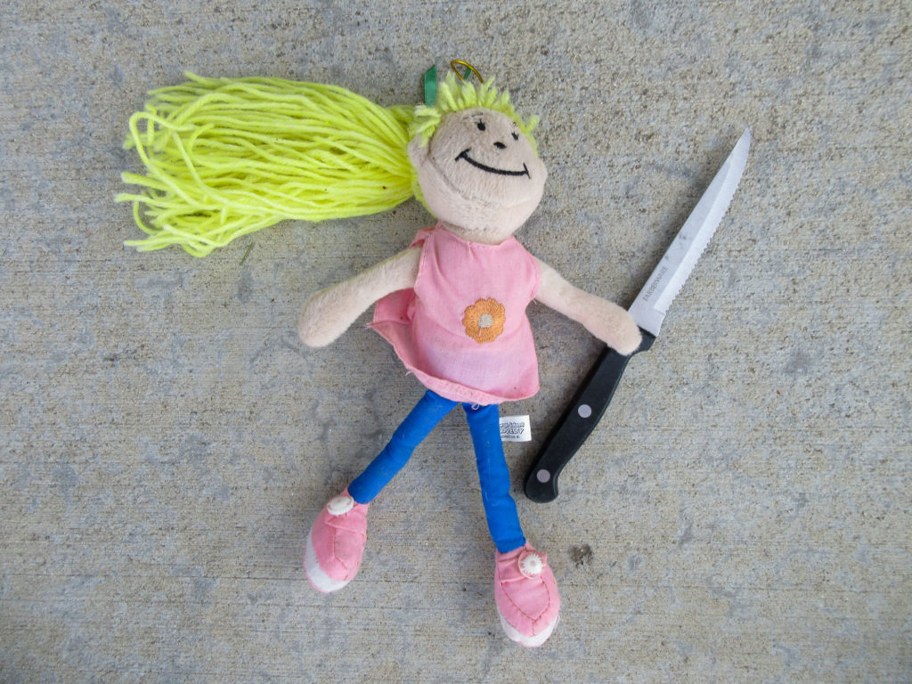 Rag doll with long blonde hair holding a steak knife