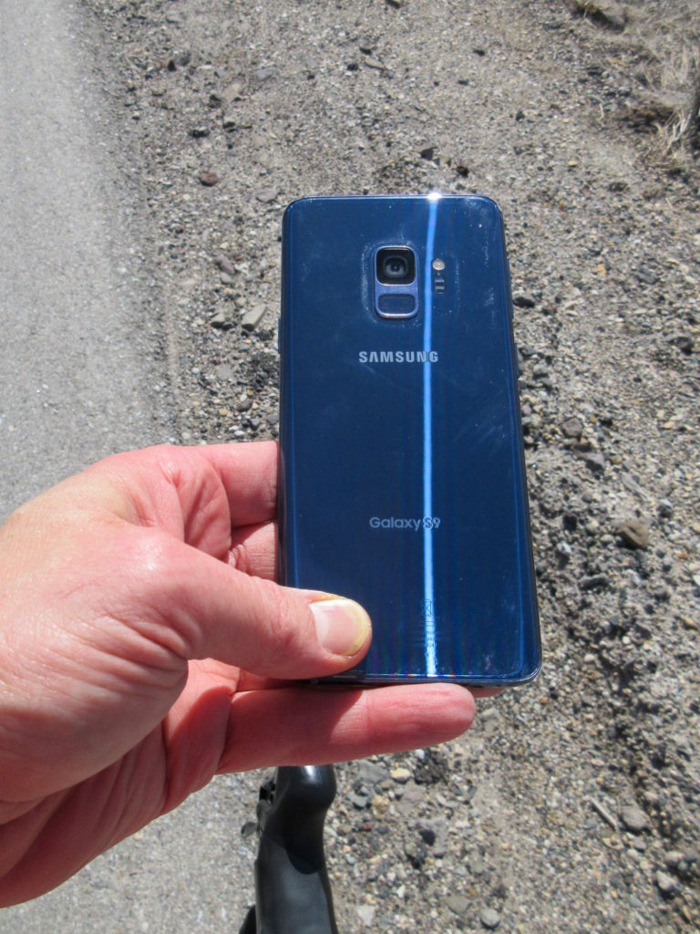 Back of a Samsung S9 shimmering in the sun held over the road shoulder