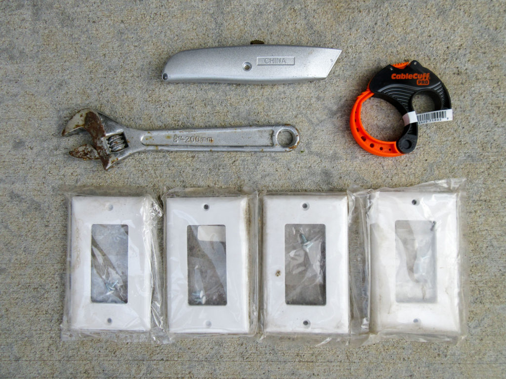 Utility knife, crescent wrench, adjustable cable tie, and four white lightswitch covers.