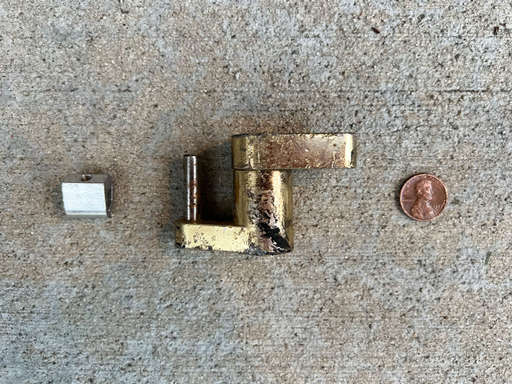 Small aluminum metal bit, brass trailer hitch coupler lock, and a penny