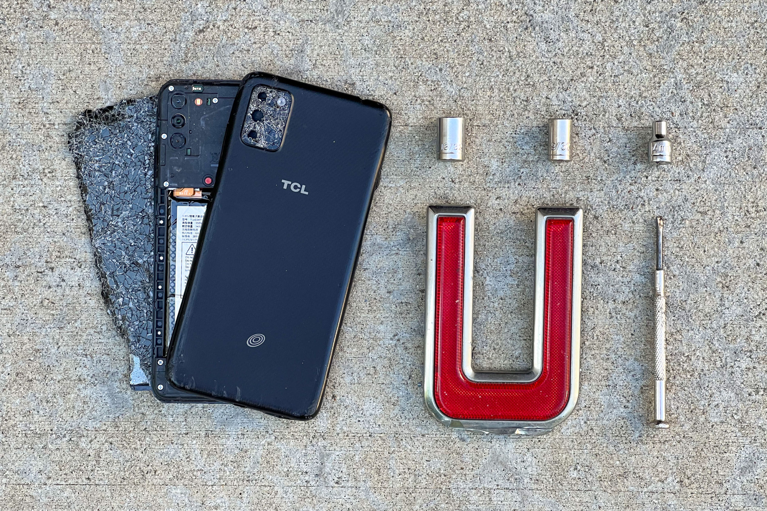 A smashed up TCL phone, three sockets, a red and chrome "U" (or rotated "C") and a micro screwdriver