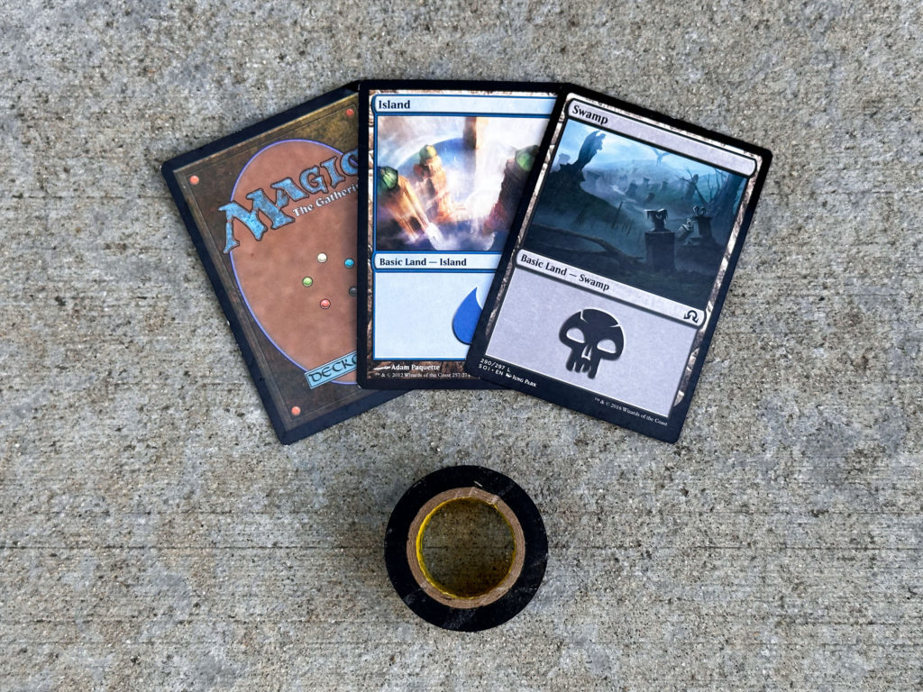 Three Magic the Gathering cards and small roll of black electrical tape