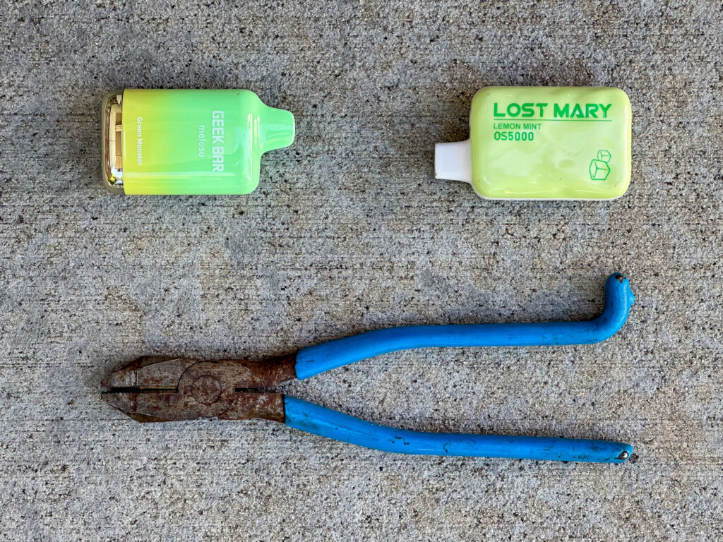 Two yellow green spent vape pods and rusted pliers with hook bend handle